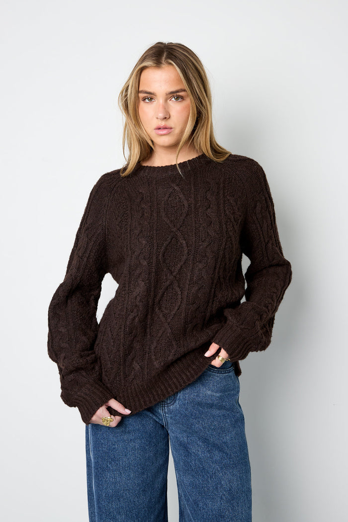 Model trägt den Elin Zopfpullover in Braun zu einer weiten blauen Jeans