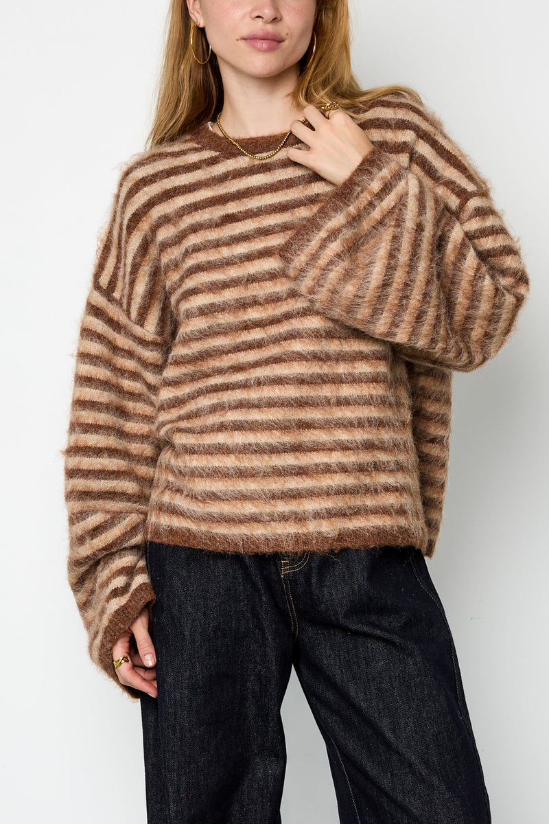 Model trägt den Mara Streifenpullover in Braun locker über einer dunklen Jeans
